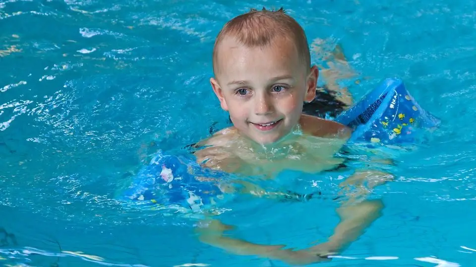 Litet barn simmar i bassäng med hjälp av armkuddar.