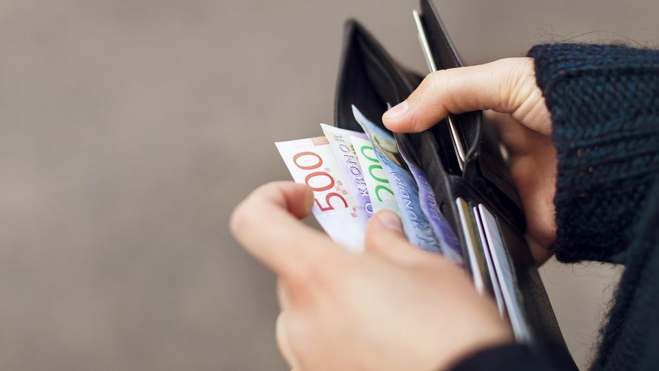 En hand bläddrar bland sedlar i olika valörer i en plånbok.
