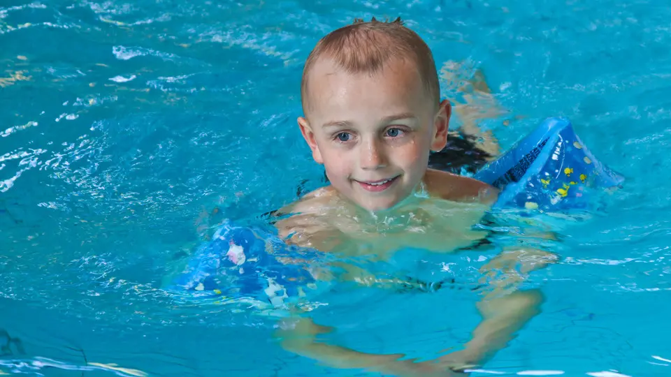 Pojke med armpuffar i simbassäng.